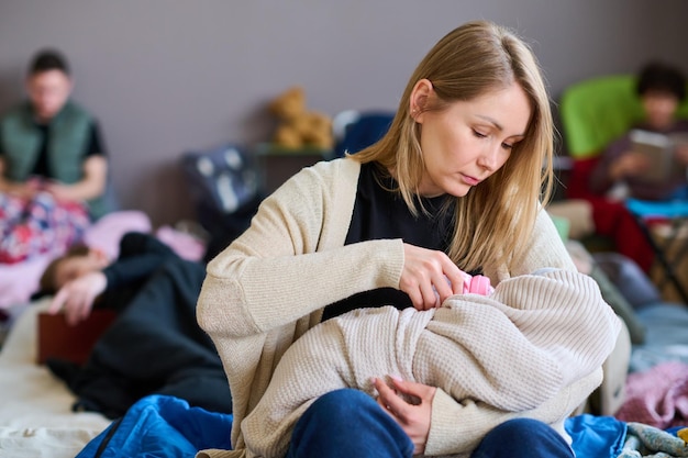 Jovem mulher com longos cabelos loiros alimentando seu bebê embrulhado em manta quente