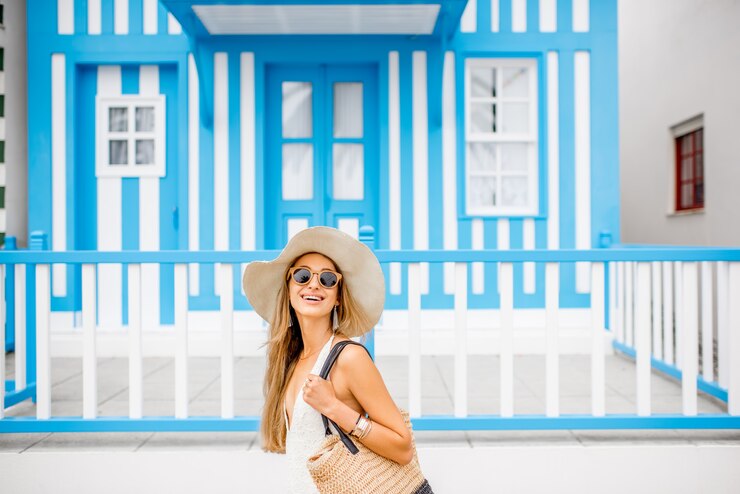 Foto jovem mulher com maiô e chapéu de sol em pé com a velha casa tradicional listrada de azul no fundo no resort da costa nova, em portugal