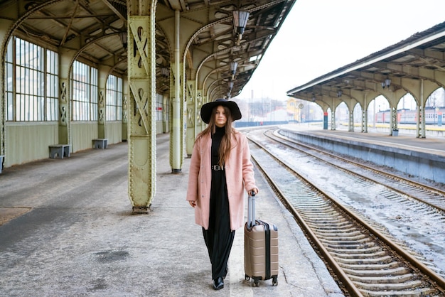 Jovem mulher com mala na plataforma da garota do viajante da estação esperando o trem, desfrutando de um fim de semana.