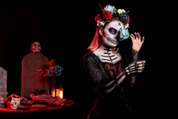 Jovem mulher com maquiagem de caveira de açúcar e rosas azuis vestidas com traje preto da morte como santa muerte. Dia da arte do corpo morto para celebrar o ritual mexicano no halloween, mito da cultura.