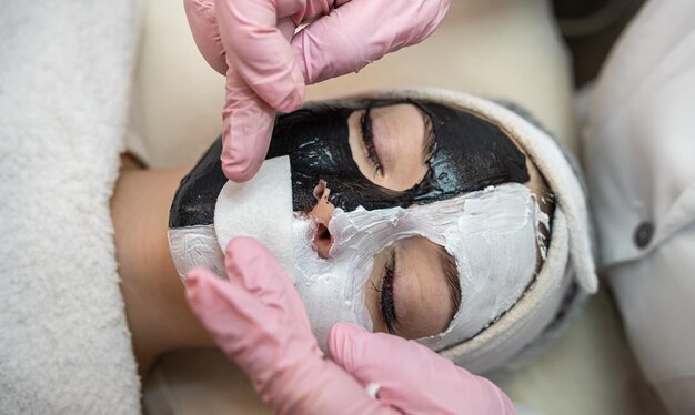 Foto jovem mulher com máscara cosmética de barro preto e branco na metade do rosto deitado um mau no salão de spa