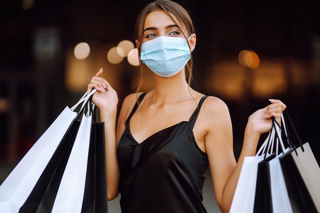 Jovem mulher com máscara médica protetora estéril no rosto com sacolas de compras, desfrutando de compras.