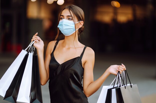 Jovem mulher com máscara médica protetora estéril no rosto com sacolas de compras, desfrutando de compras.