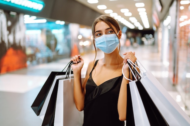 Jovem mulher com máscara médica protetora estéril no rosto com sacolas de compras no shopping.