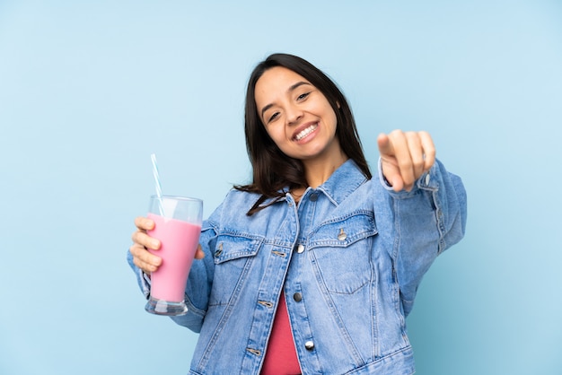 Jovem mulher com milk-shake de morango aponta o dedo para você enquanto sorrindo