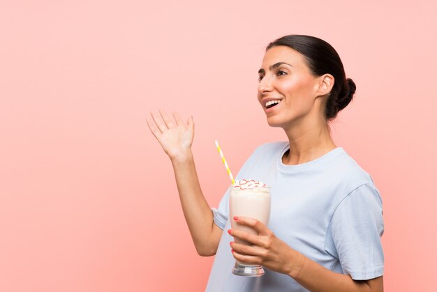 Jovem mulher com milk-shake de morango isolado parede rosa com expressão facial de surpresa