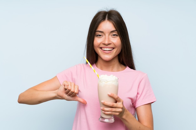 Jovem mulher com milk-shake de morango sobre parede azul isolada, orgulhoso e satisfeito