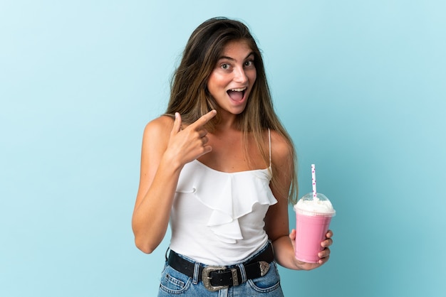 Jovem mulher com milkshake de morango isolada em azul fazendo gesto de polegar para cima