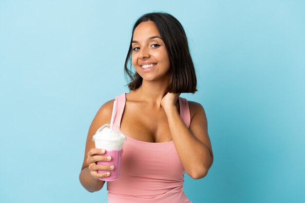 Jovem mulher com milkshake de morango isolada em um fundo azul rindo