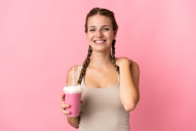 Jovem mulher com milkshake de morango isolada em um fundo rosa rindo