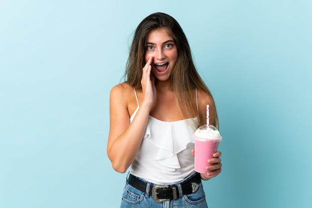 Jovem mulher com milkshake de morango isolada no azul com expressão facial surpresa e chocada