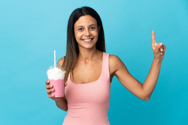 Jovem mulher com milkshake de morango mostrando e levantando um dedo em sinal dos melhores