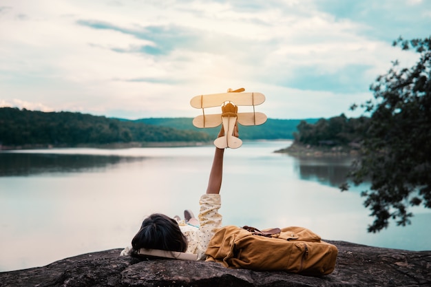 Jovem mulher com mochila e avião modelo à beira do lago