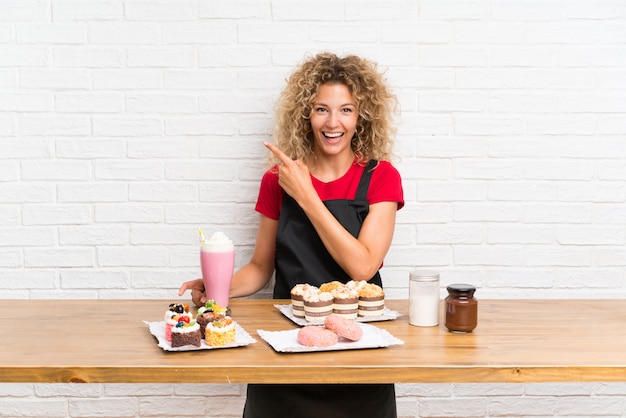 Jovem mulher com muitos mini bolos diferentes em uma mesa, apontando o dedo para o lado