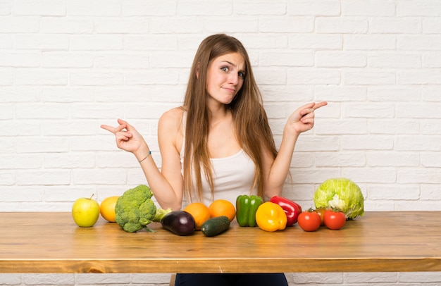 Jovem mulher com muitos vegetais apontando para as laterais tendo dúvidas