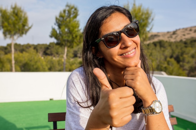 Jovem mulher com óculos de sol, fazendo o gesto de ok