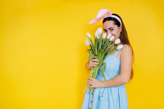 jovem mulher com orelhas de coelho no dia de páscoa segurando flores tulipa branca em um fundo amarelo