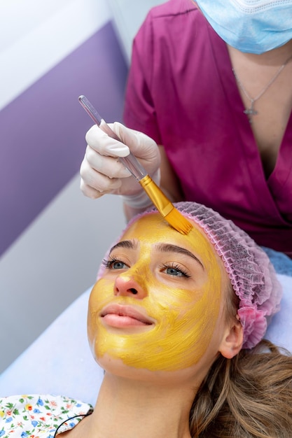 Jovem mulher com os olhos fechados e a máscara dourada no rosto, deitada no sofá na clínica de beleza, procedimento de spa.