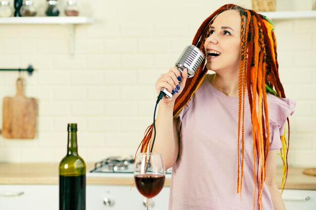 Jovem mulher com penteado brilhante com microfone retrô na cozinha Retrato de cantora com dreadlocks cantando no microfone em casa