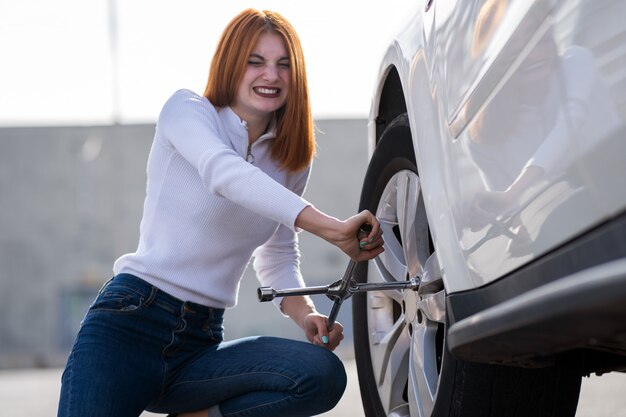 Jovem mulher com roda de mudança da chave em um carro quebrado.