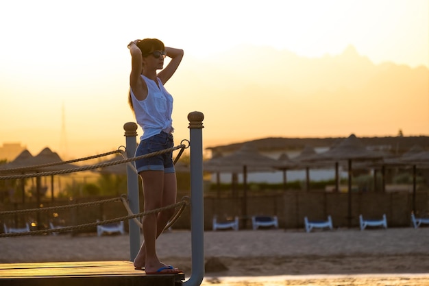 Jovem mulher com roupa casual, relaxante na beira-mar, numa noite quente. Férias de verão e conceito de viagem.