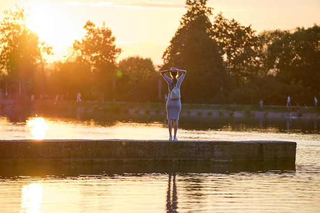 Jovem mulher com roupa casual, relaxante no lado do lago, numa noite quente. Férias de verão e conceito de viagem.