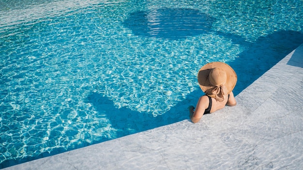 Jovem mulher com roupa de natação preta na piscina no conceito de viagens de resort de luxo e capa de banner b