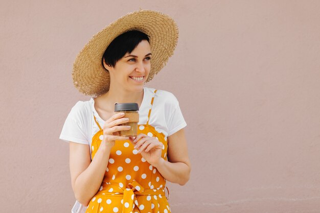 Jovem mulher com roupas de verão amarelo com um saco Eco de frutas e uma caneca de café reutilizável.