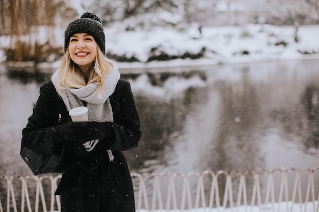 Jovem mulher com roupas quentes desfrutando na neve com uma xícara de café para viagem