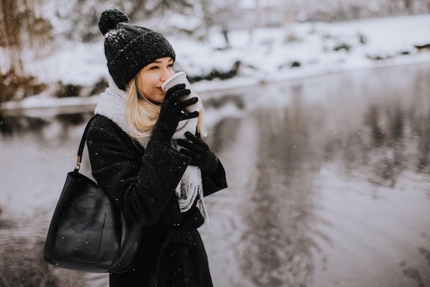 Jovem mulher com roupas quentes desfrutando na neve com uma xícara de café para viagem