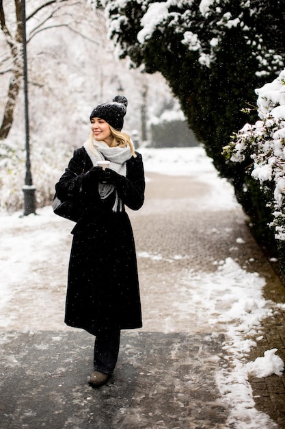 Jovem mulher com roupas quentes desfrutando na neve com uma xícara de café para viagem