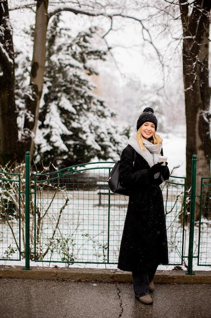 Jovem mulher com roupas quentes na neve fria do inverno bebendo café para ir