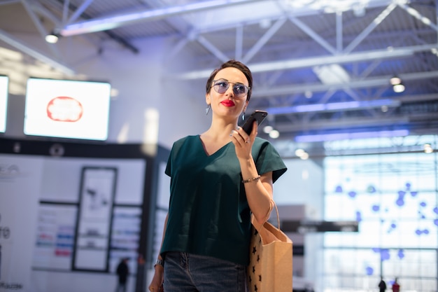 Jovem mulher com sacos de compras usando seu telefone inteligente para comprar