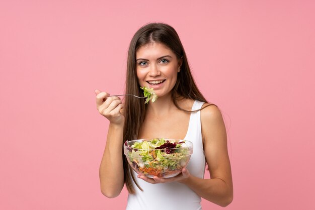 Jovem mulher com salada isolado parede rosa