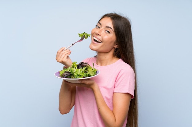 Foto jovem mulher com salada sobre fundo azul isolado