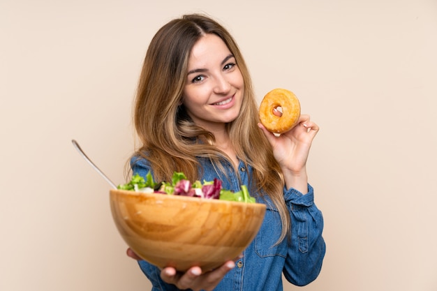 Jovem mulher com salada sobre parede isolada e segurando um donut