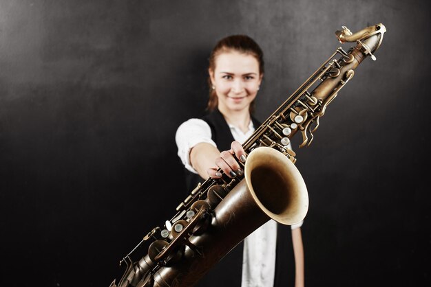 Jovem mulher com saxofone em fundo preto