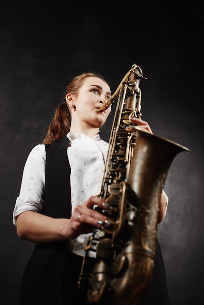 Jovem mulher com saxofone em fundo preto