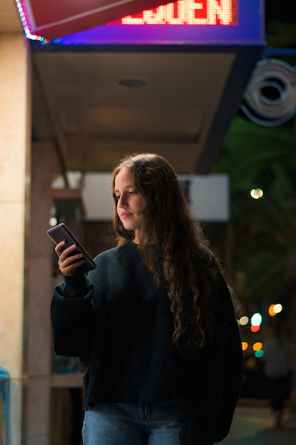 Jovem mulher com seu celular andando na rua à noite