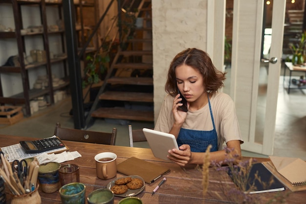 Jovem mulher com smartphone de ouvido olhando para a tela do tablet