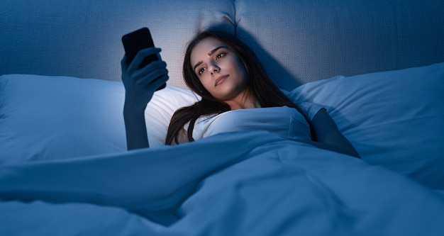 Jovem mulher com smartphone deitada na cama