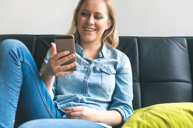 Jovem mulher com telefone no sofá em casa