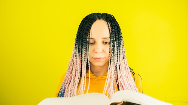 Jovem mulher com tranças senegalesas lendo livro Mulher bonita com penteado multicolorido em pé e lendo livro