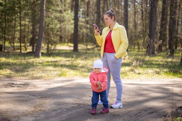 Jovem mulher com um bebê falando emocionalmente em um telefone celular em uma floresta fora da cidade