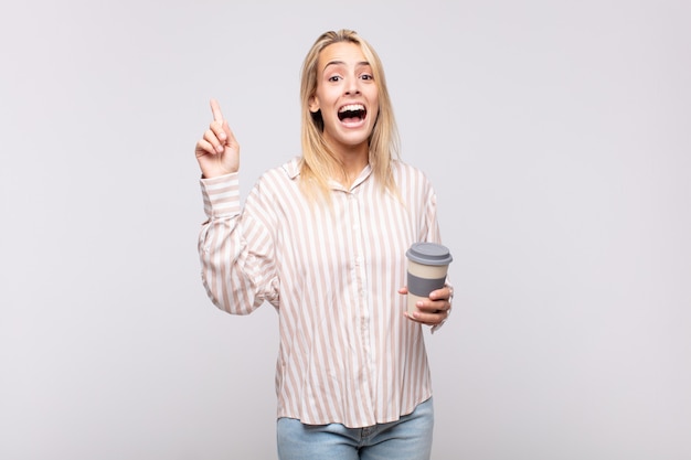 Jovem mulher com um café sentindo-se um gênio feliz e empolgado depois de realizar uma ideia, levantando alegremente o dedo, eureka!