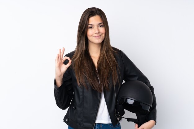 Jovem mulher com um capacete de moto sobre parede branca isolada, mostrando um sinal de ok com os dedos