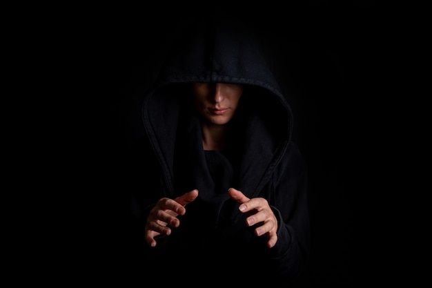 Jovem mulher com um capuz preto, mãos segurando um objeto redondo invisível em um fundo preto.