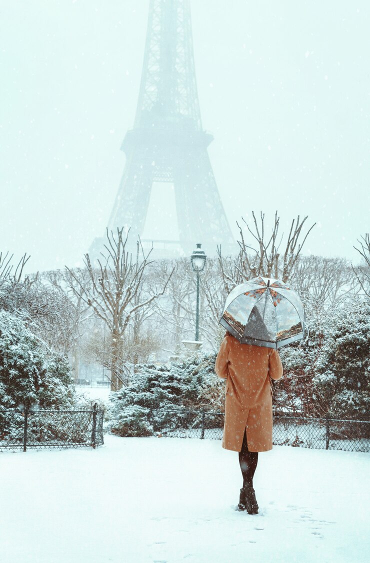 Foto jovem mulher com um casaco bege caminha sob um guarda-chuva em um inverno nevado paris