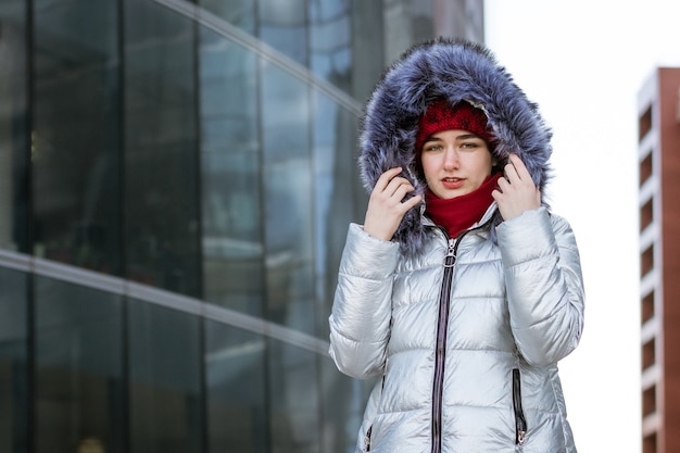 Jovem mulher com um chapéu vermelho e uma jaqueta cinza de inverno na rua se passando perto do prédio.