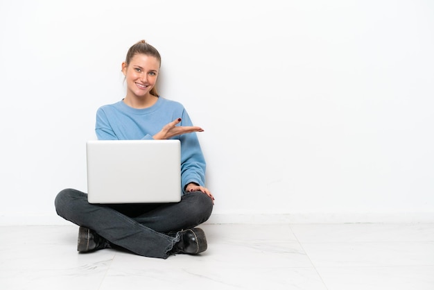 Jovem mulher com um laptop sentada no chão apresentando uma ideia enquanto olha sorrindo para